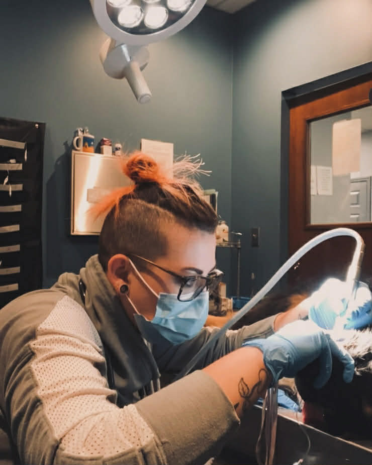 Brianna Bouchie in mask and gloves performing a dental procedure under a surgical light