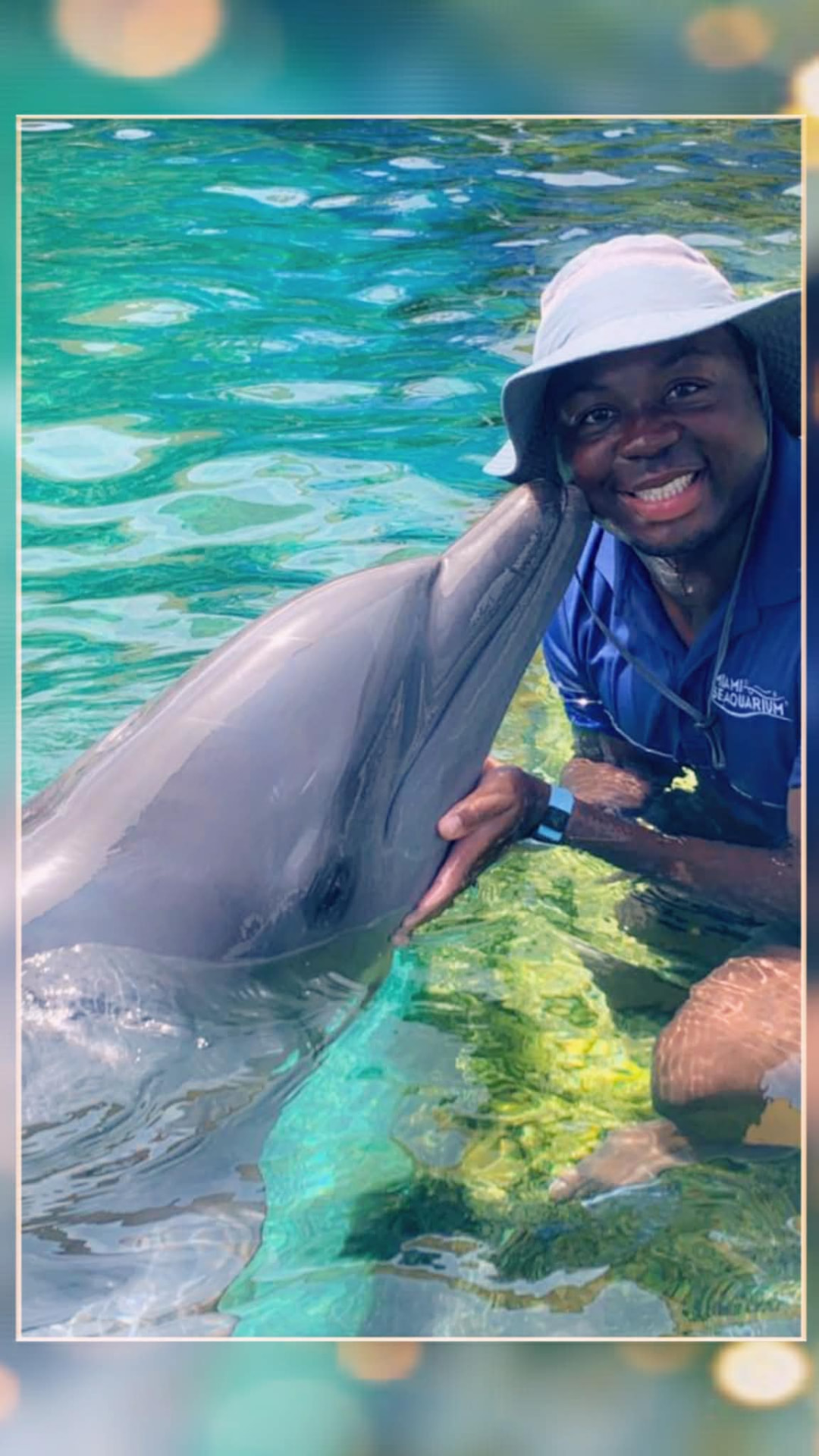 Marine mammal credentialed veterinary technician in a sun hat smiling beside a bottlenose dolphin in a lagoon